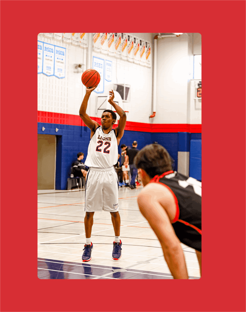 Un joueur de basket-ball portant un maillot blanc avec le numéro 22 tire un lancer franc dans un gymnase, tandis qu'un autre joueur portant un maillot noir attend à la touche. Des bannières sont accrochées au mur à l'arrière-plan.