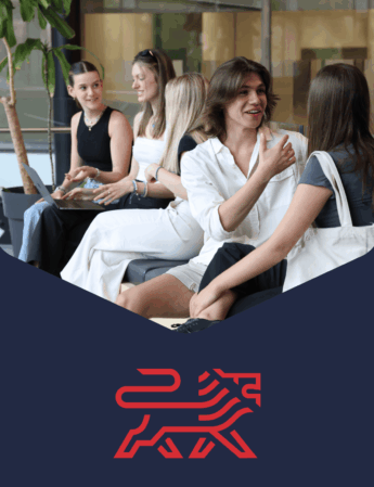 Four young adults sit together indoors, smiling and talking in a relaxed setting. A red stylized lion logo appears below them on a dark blue background.