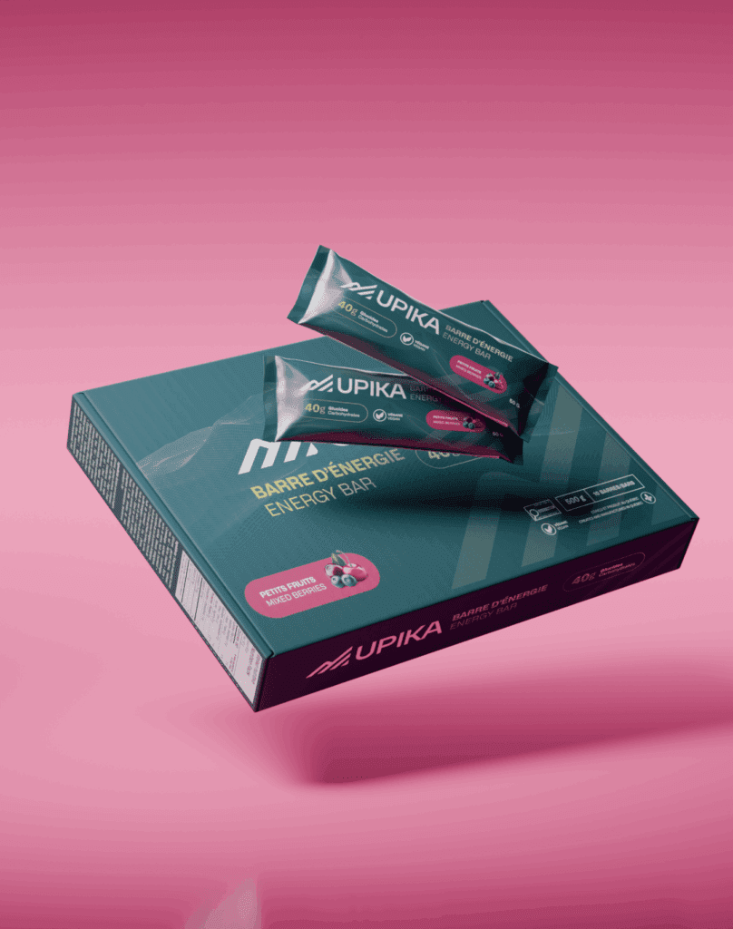 Une boîte sarcelle de barres énergétiques Upika avec deux barres individuelles présentées sur le dessus, sur un fond rose dégradé. L'emballage présente un graphisme sportif et un texte en français et en anglais.